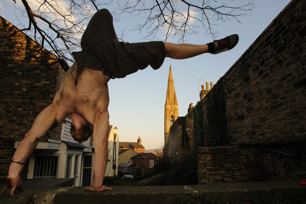 Traceur holding a one-handed balance beside a stone wall